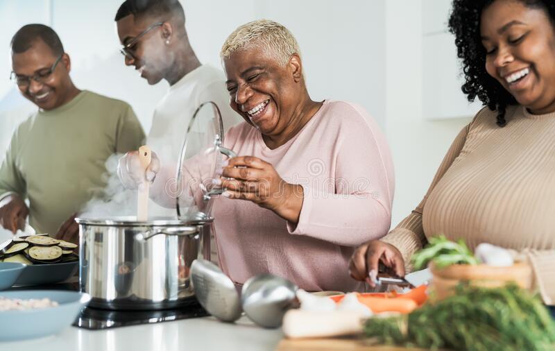 Four people smiling and laughing as they prep food in front of a steaming pot.